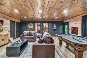 Ein Zimmer mit Holzwänden, einem Billardtisch, Ledersofas und einem Fernseher.