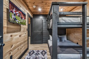 Ein Mehrbettzimmer mit einem an der Wand befestigten Fernseher, einer Tür und einem gemusterten Teppich.