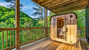 A wooden cabin with a curved entrance, a deck, and a view of a forested hillside. - Wellness & Wilderness - 3b/3.5 bath Family Retreat (Sevierville)