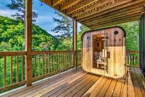 A wooden cabin with a curved entrance, a deck, and a view of a forested hillside. - Wellness & Wilderness - 3b/3.5 bath Family Retreat (Sevierville)