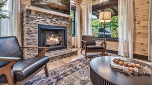A cozy room with a stone fireplace, leather chairs, a round table, and a view of the outdoors. - Wellness & Wilderness - 3b/3.5 bath Family Retreat (Sevierville)