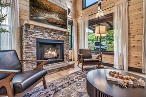 A cozy room with a stone fireplace, leather chairs, a round table, and a view of the outdoors. - Wellness & Wilderness - 3b/3.5 bath Family Retreat (Sevierville)