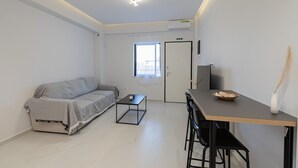 A minimalist room with a sofa, a small table, a TV, and a door leading to another room. - Dimitra Home by Rentals Pro - Polychrono Halkidiki (Polychrono)