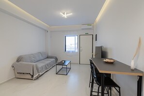 Ein schlicht eingerichteter Raum mit einer Couch, einem kleinen Tisch, einem Fernseher und einer Tür zu einem weiteren Raum.