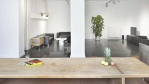 A modern interior with a wooden table, a potted plant, and a kitchen area in the background. - Modern 170 m² Loft with Sunny Terrace & Free Parking Near Alexanderplatz (Berlin)