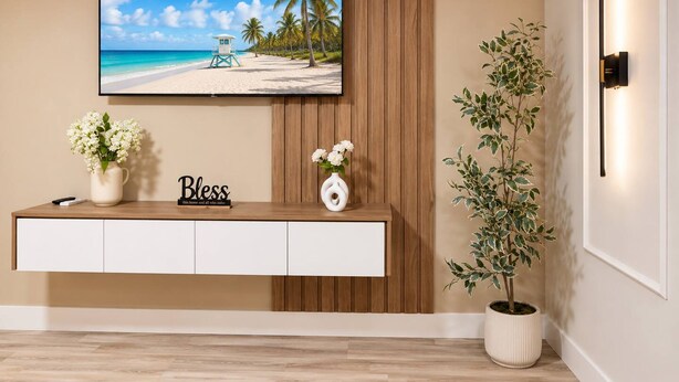 Una sala de estar con un televisor instalado en la pared, una consola de madera con un florero y una planta en maceta, además de una lámpara fijada a la pared.