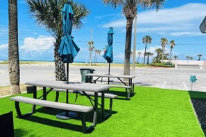 Outdoor picnic tables with umbrellas, palm trees, and a view of the beach.
