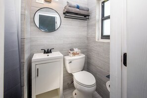 A bathroom with a white sink, a toilet, a round mirror, and a towel rack.