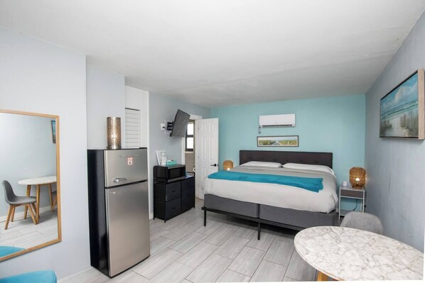 A compact hotel room with a bed, a desk, a refrigerator, and a small table.