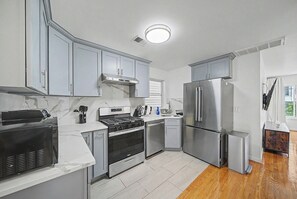 A modern kitchen with stainless steel appliances, white marble countertops, and grey cabinetry. - Luxury Turnkey Living: 3BR/2BA Near Transit (Harrison)