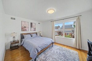 A bedroom with a bed, bedside tables, a window with curtains, and artwork on the wall. - Luxury Turnkey Living: 3BR/2BA Near Transit (Harrison)