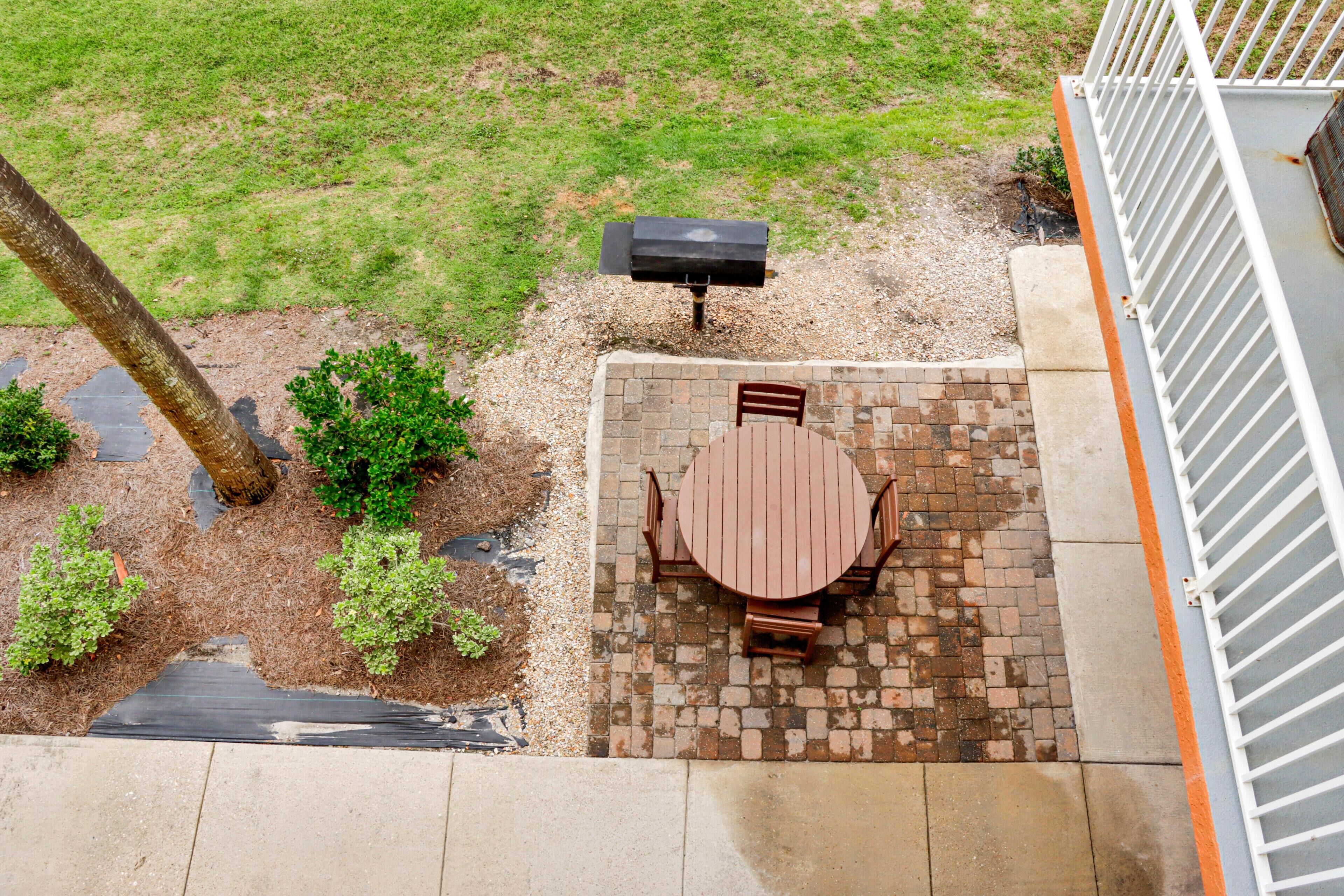 A patio with a brick table and chairs, a grill, and a small garden area with a tree and shrubs.