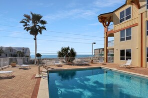 Ein Swimmingpool mit Liegestühlen, einer Palme und Blick auf das Meer.