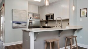 A modern kitchen with white cabinets, stainless steel appliances, and a large island with stools. - Summerhouse 206 - Brown Eyed Girl (Port St. Joe)