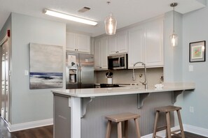 A modern kitchen with white cabinets, stainless steel appliances, and a large island with stools. - Summerhouse 206 - Brown Eyed Girl (Port St. Joe)