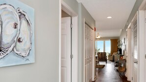 A hallway with white doors, a ceiling fan, and a view into a living room with a couch and a table. - Summerhouse 206 - Brown Eyed Girl (Port St. Joe)