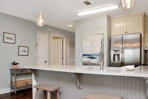 A kitchen with a stainless steel refrigerator, a white countertop, and a hanging light fixture. - Summerhouse 206 - Brown Eyed Girl (Port St. Joe)