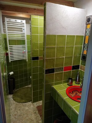 Uma casa de banho com azulejos verdes, um suporte de toalhas branco, uma pia vermelha e um espelho pequeno.