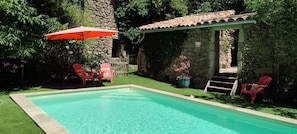 Piscina com muro de pedra e pérgola de madeira.