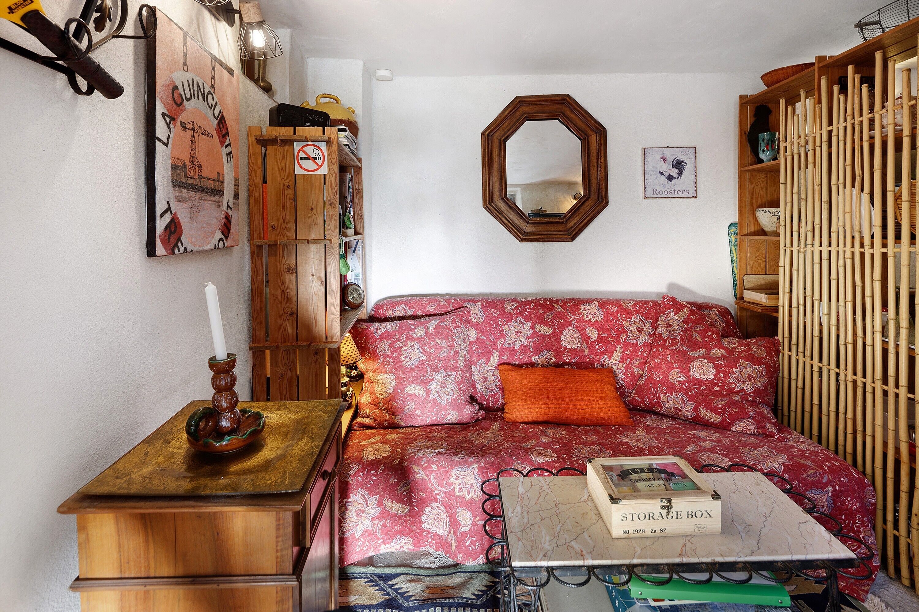A bedroom with a floral bedspread, a storage box, a wooden cabinet, and a mirror on the wall.