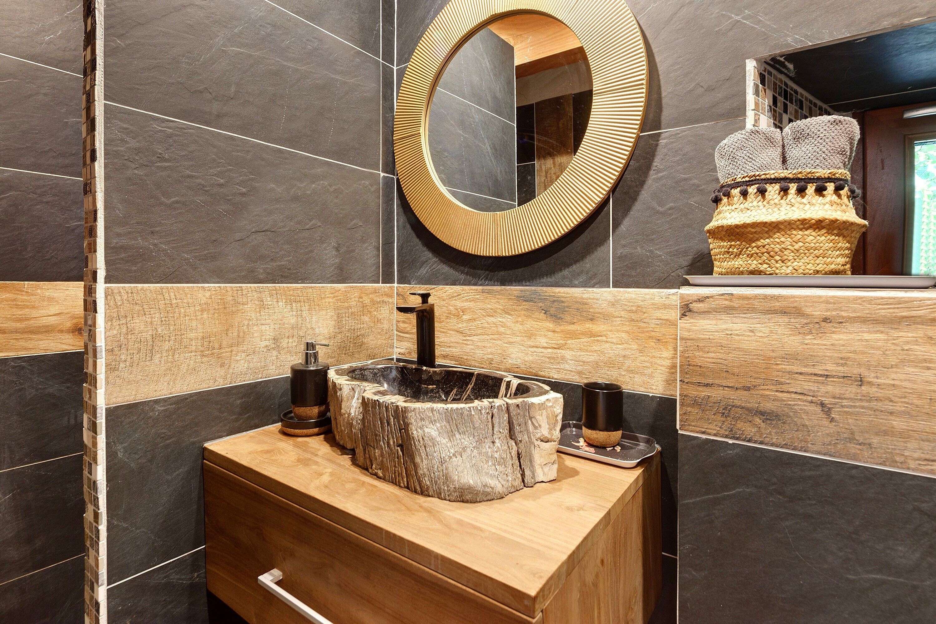 A bathroom with a wooden vanity, a round mirror, and a stone basin.