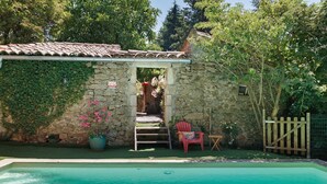 Ein Steinhaus mit Pool, einem Holztor und einem roten Stuhl.