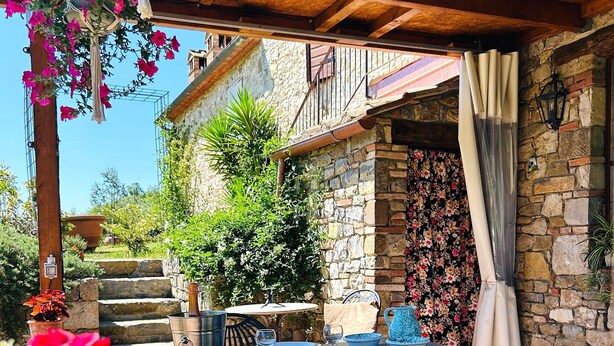 Eine Terrasse mit Tisch und Stühlen, eine Steinwand mit floralem Muster und eine Holzdeckenkonstruktion.