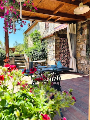 Eine Terrasse mit Tisch und Stühlen, eine Steinwand mit floralem Muster und eine Holzdeckenkonstruktion.