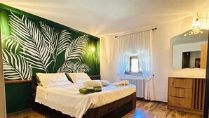 Ein Schlafzimmer mit einem Bett, einer Kommode, einem Fenster mit Vorhängen, einem Heizkörper und einer Wand mit Blättermuster.