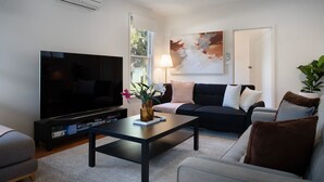 A living room with a flat-screen TV, a coffee table with a vase, a sofa with cushions, and a potted plant. - Hepburn Woodland Retreat (Dry Diggings)