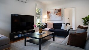 A living room with a flat-screen TV, a coffee table with a vase, a sofa with cushions, and a potted plant. - Hepburn Woodland Retreat (Dry Diggings)