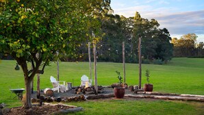 A garden with a tree, two white chairs, a wheelbarrow, and firewood. - Hepburn Woodland Retreat (Dry Diggings)