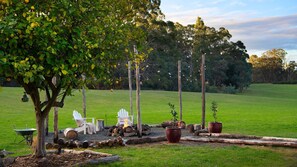 A garden with a tree, two white chairs, a wheelbarrow, and firewood. - Hepburn Woodland Retreat (Dry Diggings)
