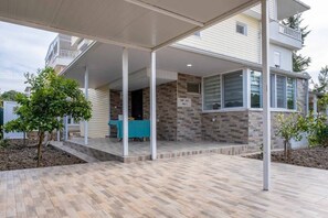 Ein überdachter Patio-Bereich mit Tisch und Stühlen, ein kleiner Garten und ein Gebäude mit einer Steinaußenwand.