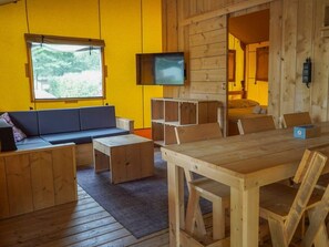 Een knus houten interieur met een bank, een tv aan de muur en een eettafel.