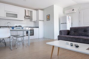 A modern kitchen with white cabinets, a dining area with a white table and metal chairs, and a gray sofa in a living area. - AMADO - 3 Bed Duplex with view on pool (Antalya)