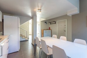 Eine moderne Küche mit weißen Schränken, einem eingebauten Backofen und einer Edelstahl-Dunstabzugshaube. Es gibt einen Essbereich mit einem weißen Tisch und Stühlen sowie eine Treppe zu einer weiteren Ebene.
