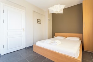 Ein Schlafzimmer mit einem hölzernen Bett, weißen Laken, einer weißen Tür und einer Lampenleiste.