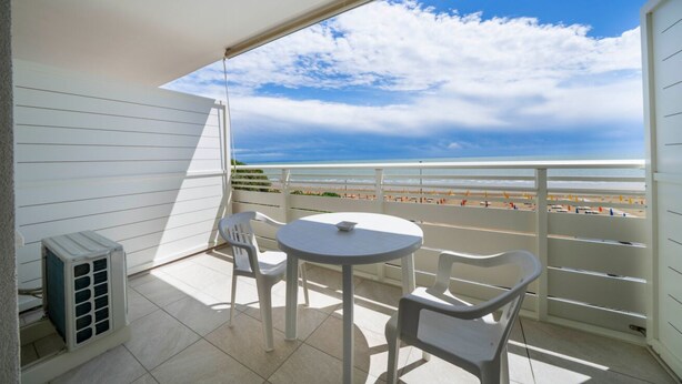 Ein Balkon mit Blick auf den Strand, einem Tisch, zwei Stühlen und einer Klimaanlage.
