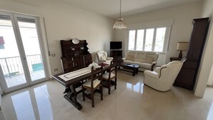 A spacious living room with a dining area, a sofa, a TV, and a balcony. - ‘Casa Vacanze Rita La California’ Apartment with Private Garden and Balcony (La California)
