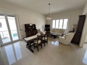 A spacious living room with a dining area, a sofa, a TV, and a balcony.
