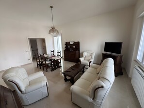 A living room with a sofa, armchair, dining table, chairs, a TV, and a chandelier. - Apartment 'Casa Vacanze Rita La California' with Private Garden and Balcony (La California)