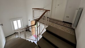 A staircase with a wooden handrail and white railings, leading to a room with a door and a radiator. - ‘Casa Vacanze Rita La California’ Apartment with Private Garden and Balcony (La California)