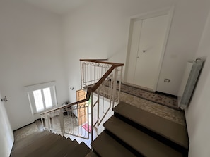 Una escalera con barandilla de madera y pasamanos blancos, que conduce a una habitación con una puerta y un radiador.