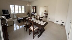 A spacious living room with a dining area, a television, and a large window. - ‘Casa Vacanze Rita La California’ Apartment with Private Garden and Balcony (La California)