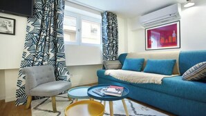 A living room with a blue sofa, a grey armchair, a small coffee table, and patterned curtains. - JUST A SHORT WALK FROM THE ICONIC CENTRE POMPIDOU- LE MARAIS (Paris)