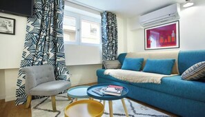 A living room with a blue sofa, a grey armchair, a small coffee table, and patterned curtains. - JUST A SHORT WALK FROM THE ICONIC CENTRE POMPIDOU- LE MARAIS (Paris)