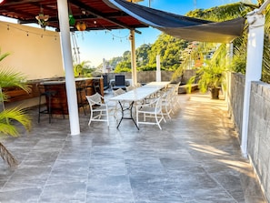 Un patio al aire libre con una mesa de comedor, sillas y una zona de bar.