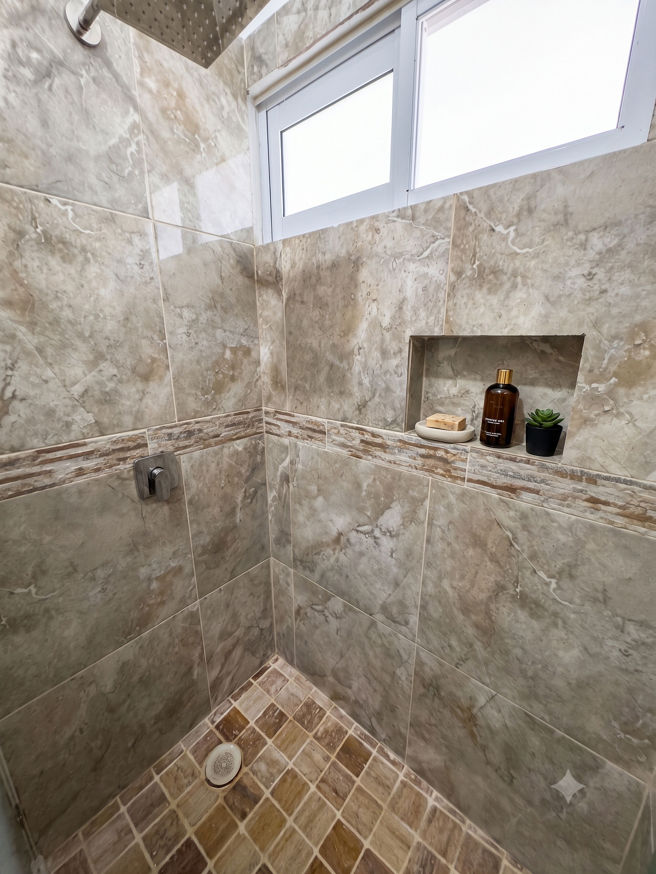 Un baño con baldosas de mármol, ducha, ventana y un estante con artículos de aseo.