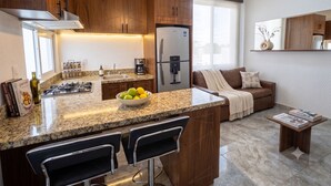 Eine moderne Küche mit Granitarbeitsplatten, Holzschränken, einem eingebauten Gasherd, einem Kühlschrank und einer Kaffeemaschine.